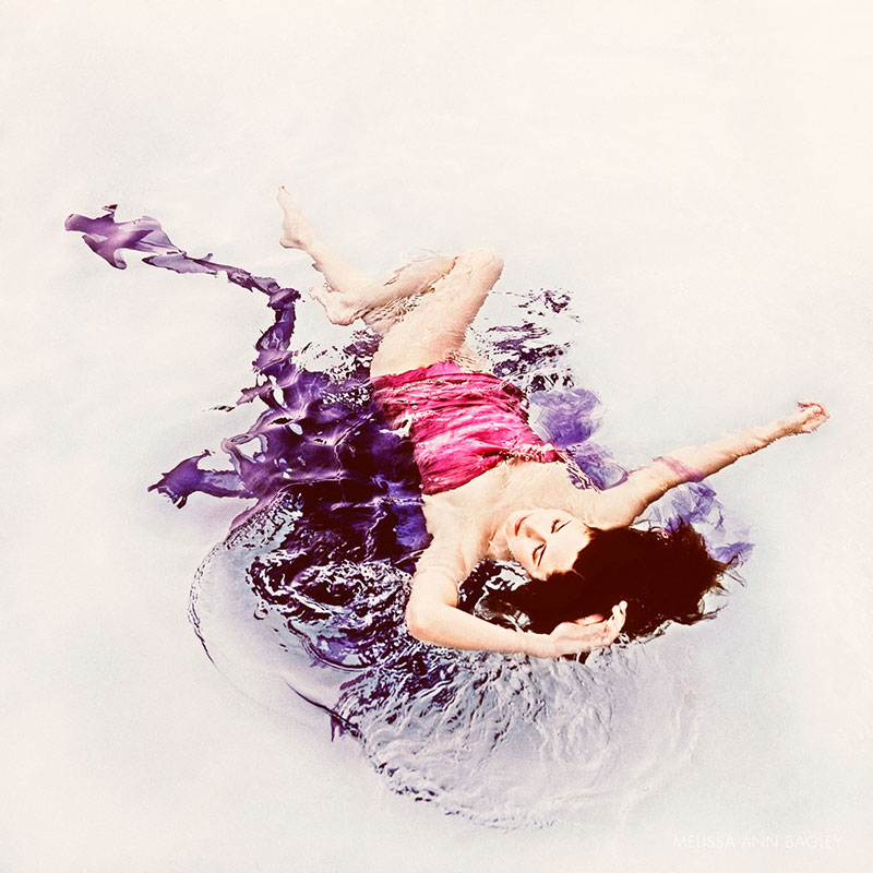 Color portrait of a woman with long dark hair in a pink bathing suit floating in a pool.