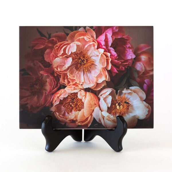 Photo of pink peonies and honeybees printed on a ceramic tile. The ceramic piece is displayed on a black tabletop easel